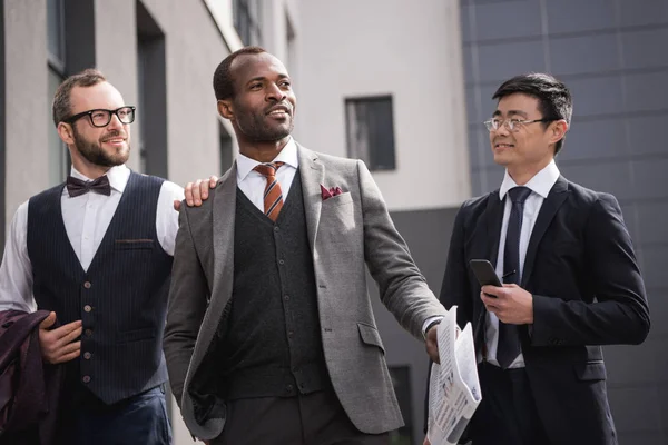 Junge stilvolle multiethnische Geschäftsleute in Formalbekleidung, die im Freien spazieren gehen, Besprechung des Geschäftsteams — Stockfoto