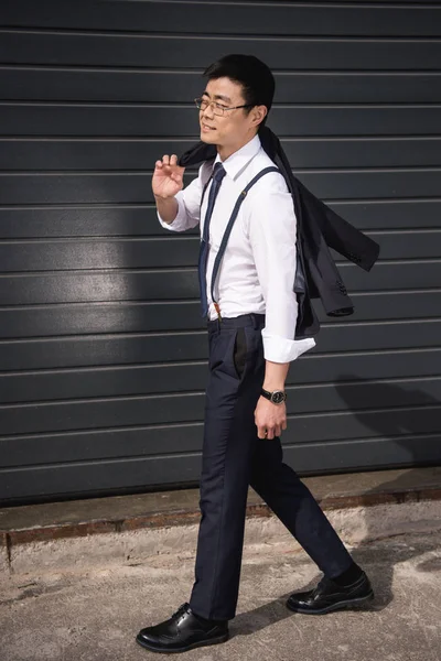 Молодой улыбающийся азиатский бизнесмен в очках прогуливаясь по улице — стоковое фото