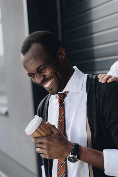 Стильный африканский американский бизнесмен смеется и держит кофе, чтобы выйти на улицу — Бесплатное стоковое фото