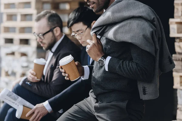 Empresários multiculturais segurando copos de café de papel e sentado ao ar livre, conceito de equipe de empresários — Fotografia de Stock