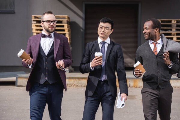 молодые многонациональные бизнесмены в формальной одежде, гуляющие на кофе-брейке на свежем воздухе, деловая встреча
