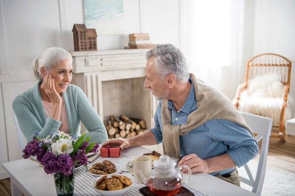 мужчина преподносит подарок жене во время завтрака
