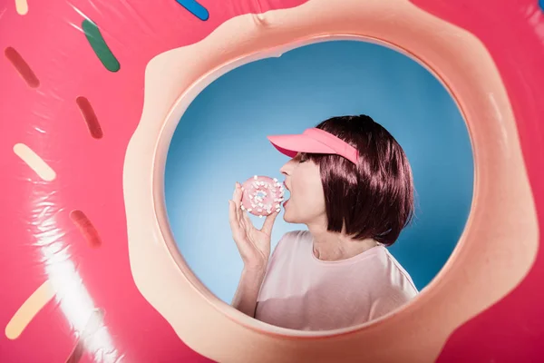 Woman eating doughnut into swimming tube — Stock Photo, Image