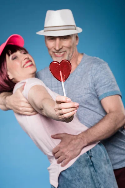 Elderly couple hugging and holding lollipop — Stock Photo, Image