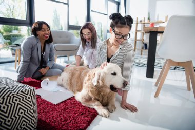 multiethnic businesswomen petting dog at office clipart