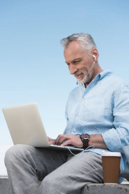 smiling senior man typing on laptop clipart