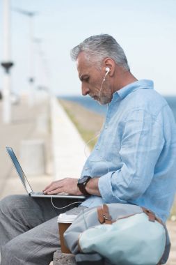 elderly man typing on laptop outdoors clipart