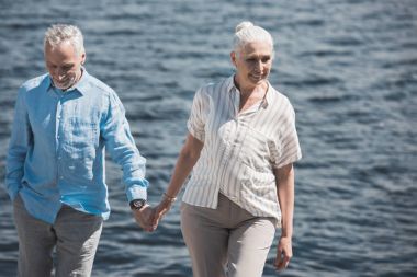 smiling elderly couple walking on riverside clipart