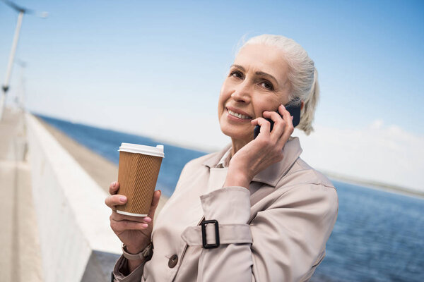 пожилая женщина разговаривает на смартфоне на набережной
