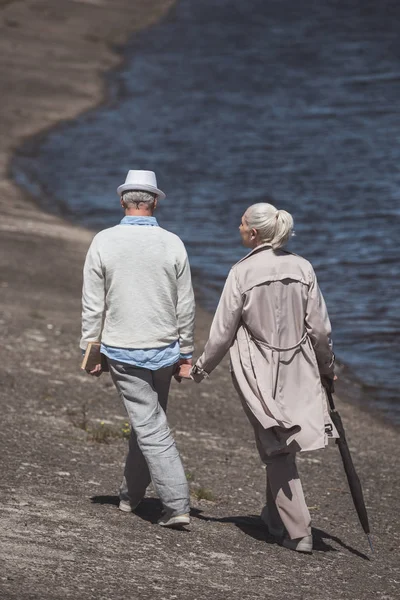 Elderly couple walking on river shore — Stock Photo, Image