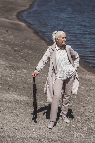 senior woman posing with umbrella on riverside