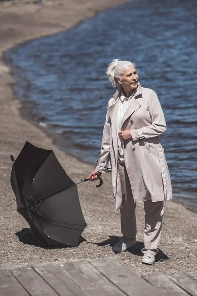 Senior woman posing with umbrella on riverside — Stock Photo, Image