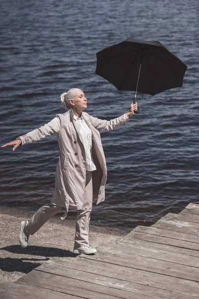 Seniorin läuft mit Regenschirm am Flussufer — Stockfoto