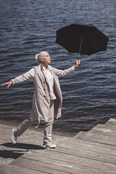 elderly woman walking with umbrella on riverside