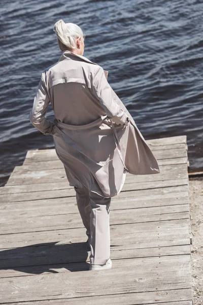 Ältere Frau im Mantel spaziert am Flussufer — Stockfoto