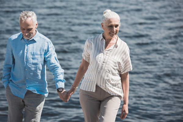 улыбающаяся пожилая пара, идущая по берегу реки
