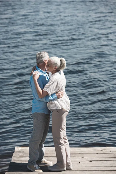 Coppia dai capelli grigi che si abbraccia sul lungofiume — Foto Stock