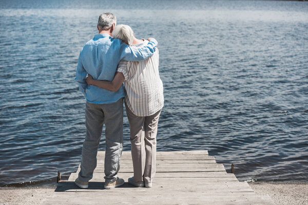 пожилая пара обнимается, стоя на берегу реки
