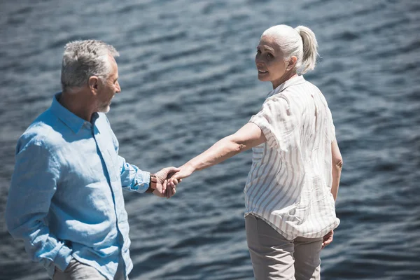 Pareja de ancianos cogidos de la mano en la orilla del río —  Fotos de Stock