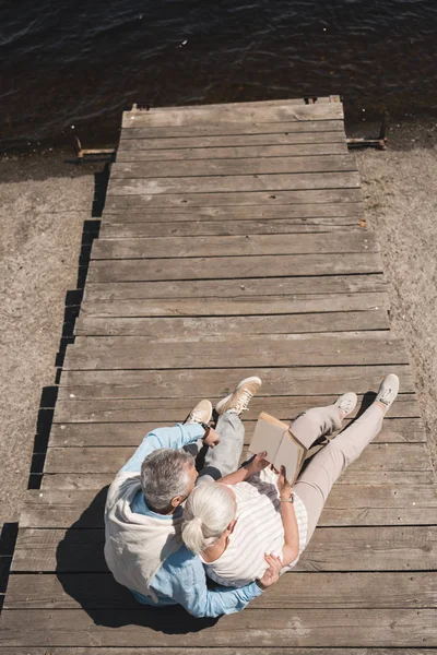 Senior couple reading book on riverside — Stock Photo, Image