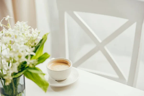 Kopp kaffe med bukett blommor på bord — Stockfoto