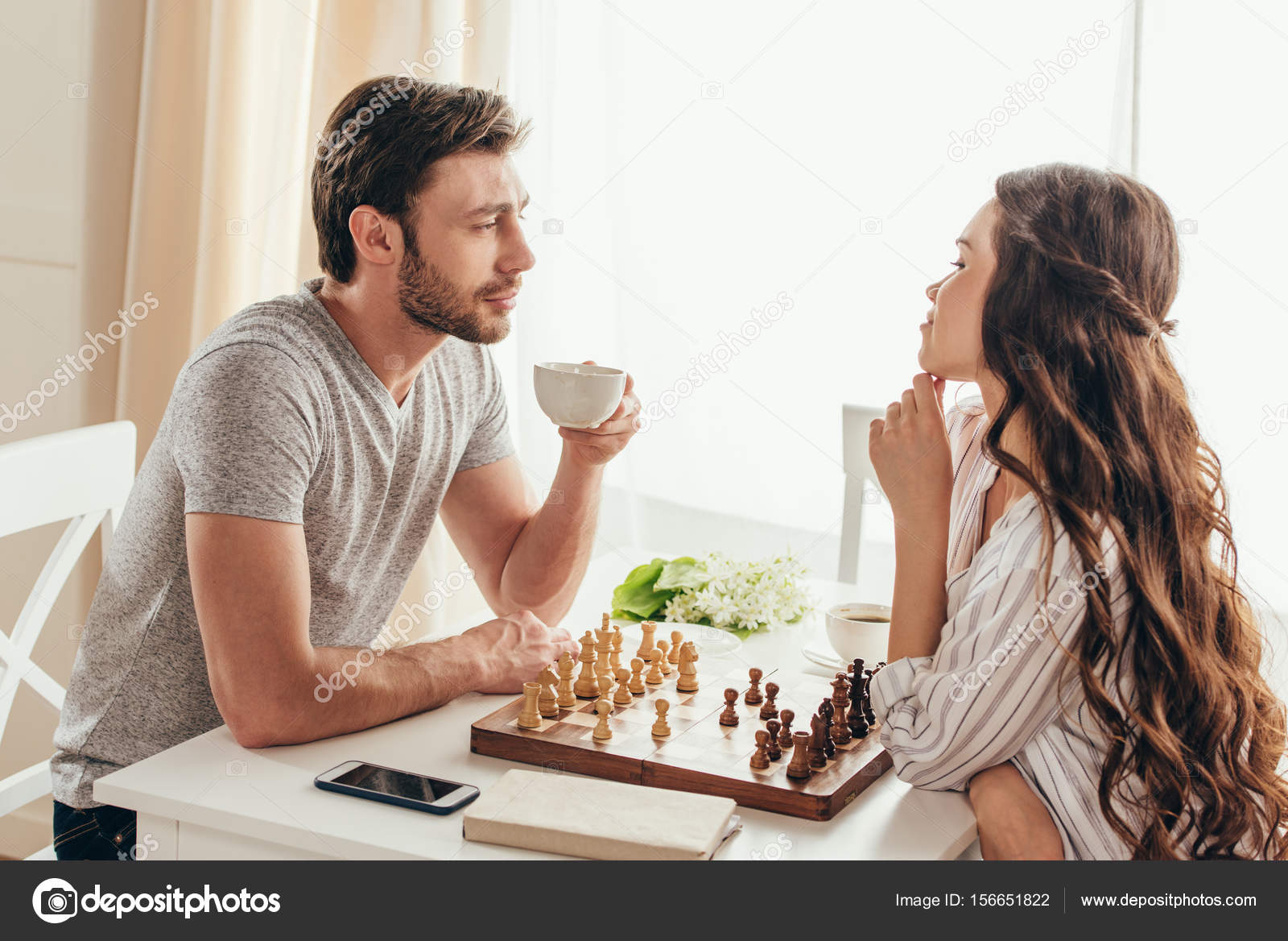 young couple playing chess while sitting at table at home - Unpacked