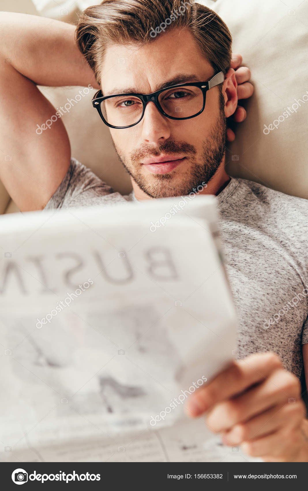 Young man in glasses reading newspaper Stock Photo by