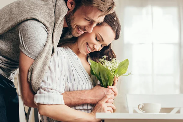 Couple hugging and holding flowers at home — Stock Photo, Image