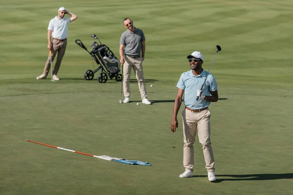 Sportsmen standing with golf clubs on pitch — Stock Photo, Image