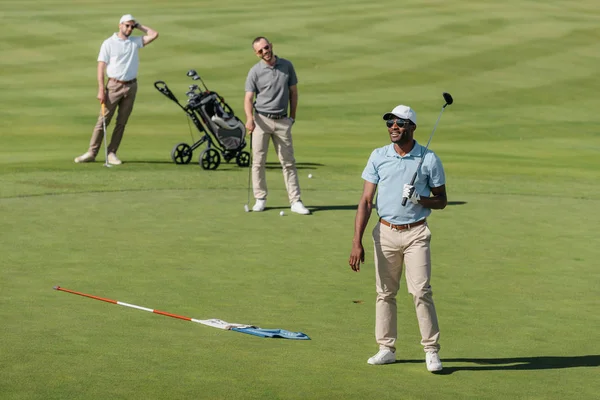 Deportistas de pie con palos de golf en el campo — Foto de Stock