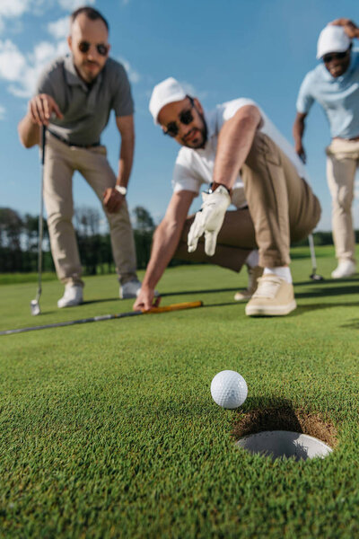 игроки в гольф смотрят на мяч возле лунки
