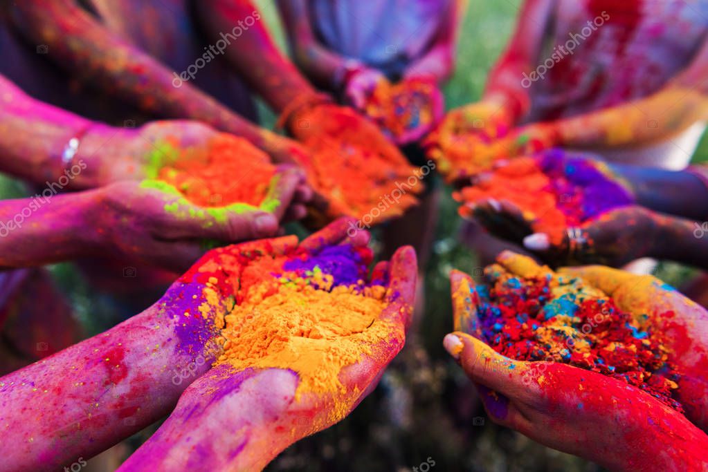 Close-up partial view of young people holding colorful powder in hands at holi festival