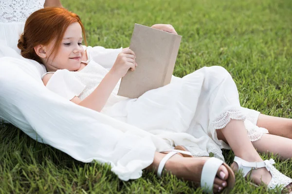 Meisje met moeder leesboek in park — Stockfoto