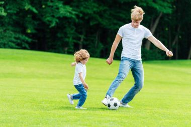 father and son playing soccer in park clipart
