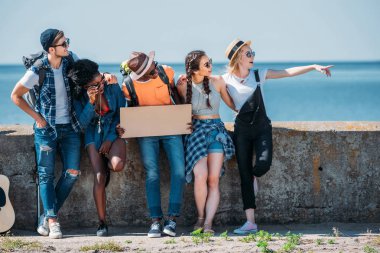 multiethnic friends pointing away while hitchhiking clipart