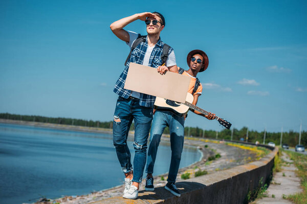 multicultural men with cardboard hitchhiking
