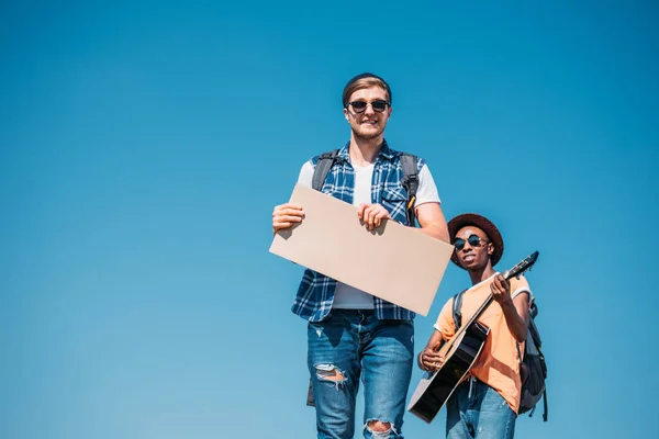 Multiethnic men with empty cardboard hitchhiking — Free Stock Photo