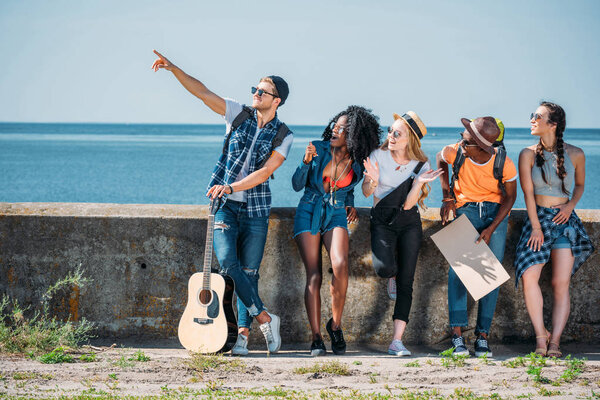 multiethnic friends pointing away while hitchhiking