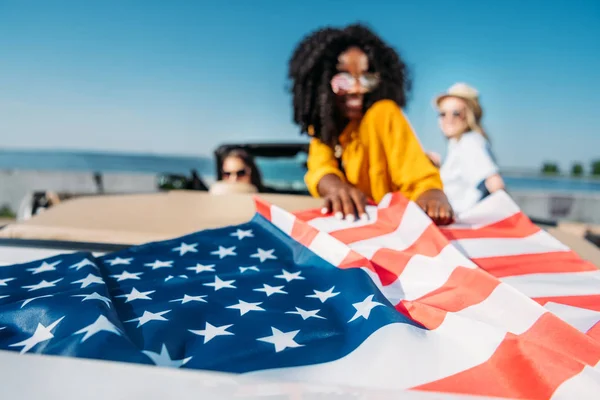 Mulheres multiétnicas no carro com bandeira americana — Fotografia de Stock