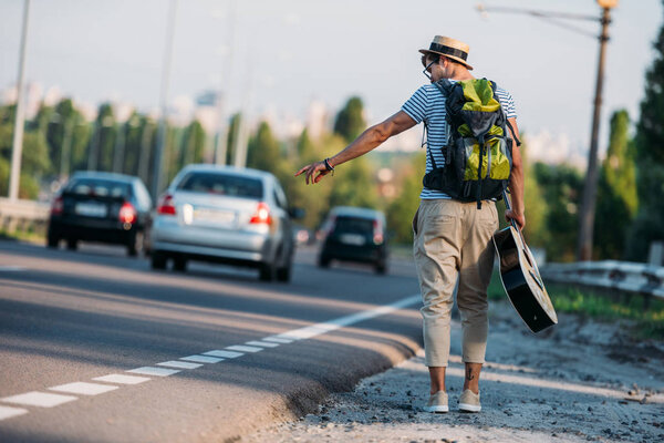 young man with guitar hitchhiking alone