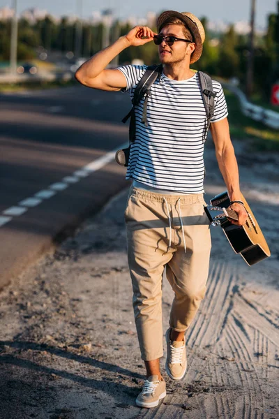 Młody człowiek z gitara hitchhiking sam — Zdjęcie stockowe