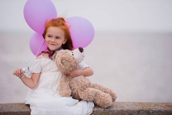 child with teddy bear and balloons