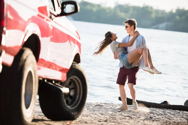 Чоловік носить дівчину на березі річки — стокове фото