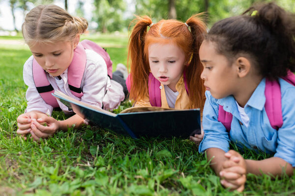 multiethnic kids reading book on grass 
