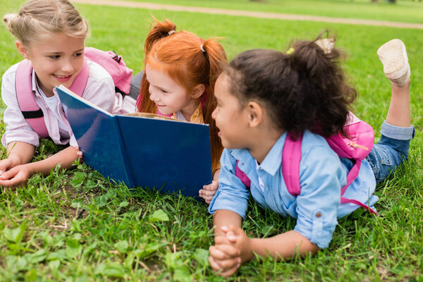 multiethnic kids reading book on grass