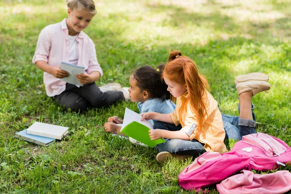 Multiethnic schoolgirls studying on grass — Free Stock Photo