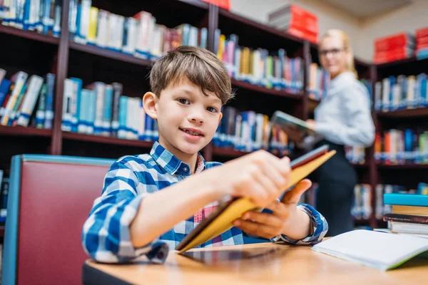 Schoolboy holding tablet in library — Stock Photo, Image
