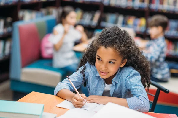 Schoolgirl doing homework in library — Stock Photo, Image