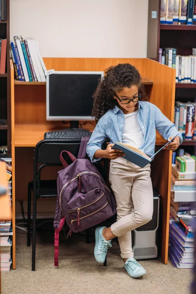 Schoolgirl reading book in library — Stock Photo, Image