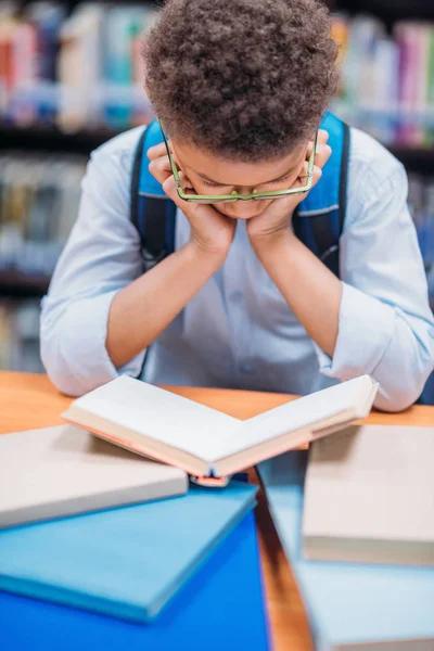 Шкільний хлопець читає книгу в бібліотеці — стокове фото